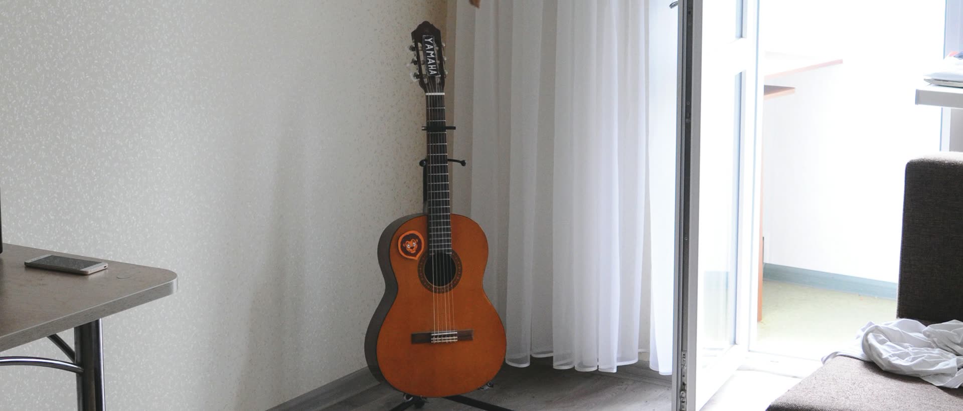 A bright, compact apartment room with a guitar and an open balcony door